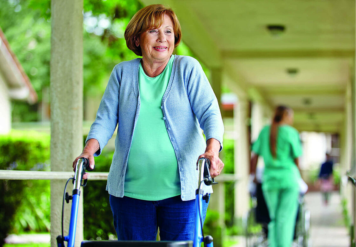 Seniorin läuft am Rollator vor einem Pflegeheim