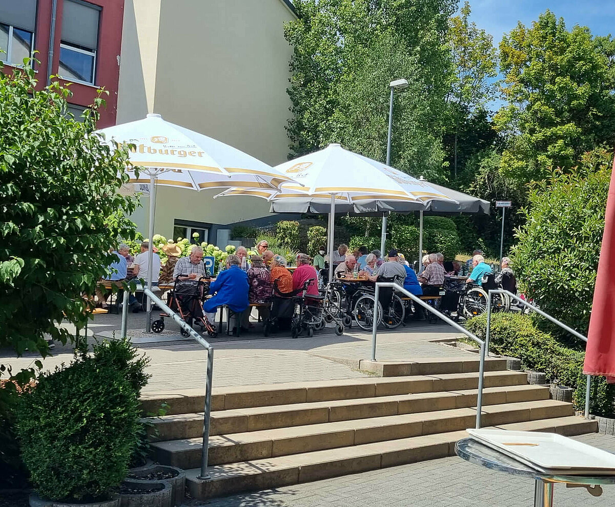 Bewohnerinnen und Bewohner sitzen unter Sonnenschirmen und feiern das Sommerfest