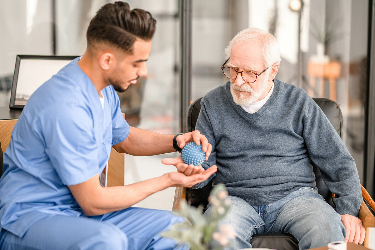 Auszubildender im Pflegeheim hilft Senior mit Ball bei der Beweglichkeit