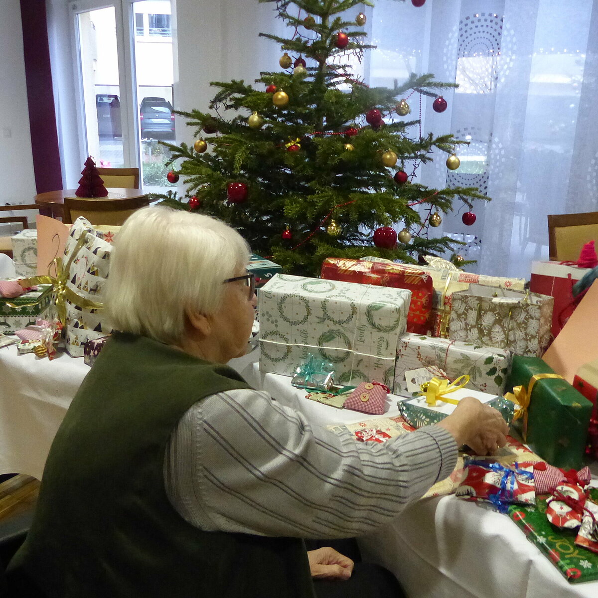 Christel Bühlen vor einem Tisch mit eingepackten Geschenken, im Hintergrund ein geschmückter Weihnachtsbaum