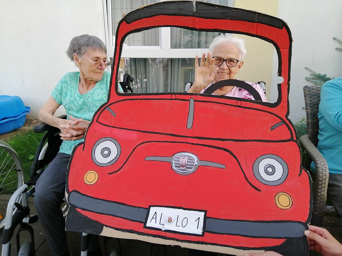 Bewohnerinnen hinter Papp-Auto bei der italienischen Woche - Rom im Seniorenzentrum AGO Trier 