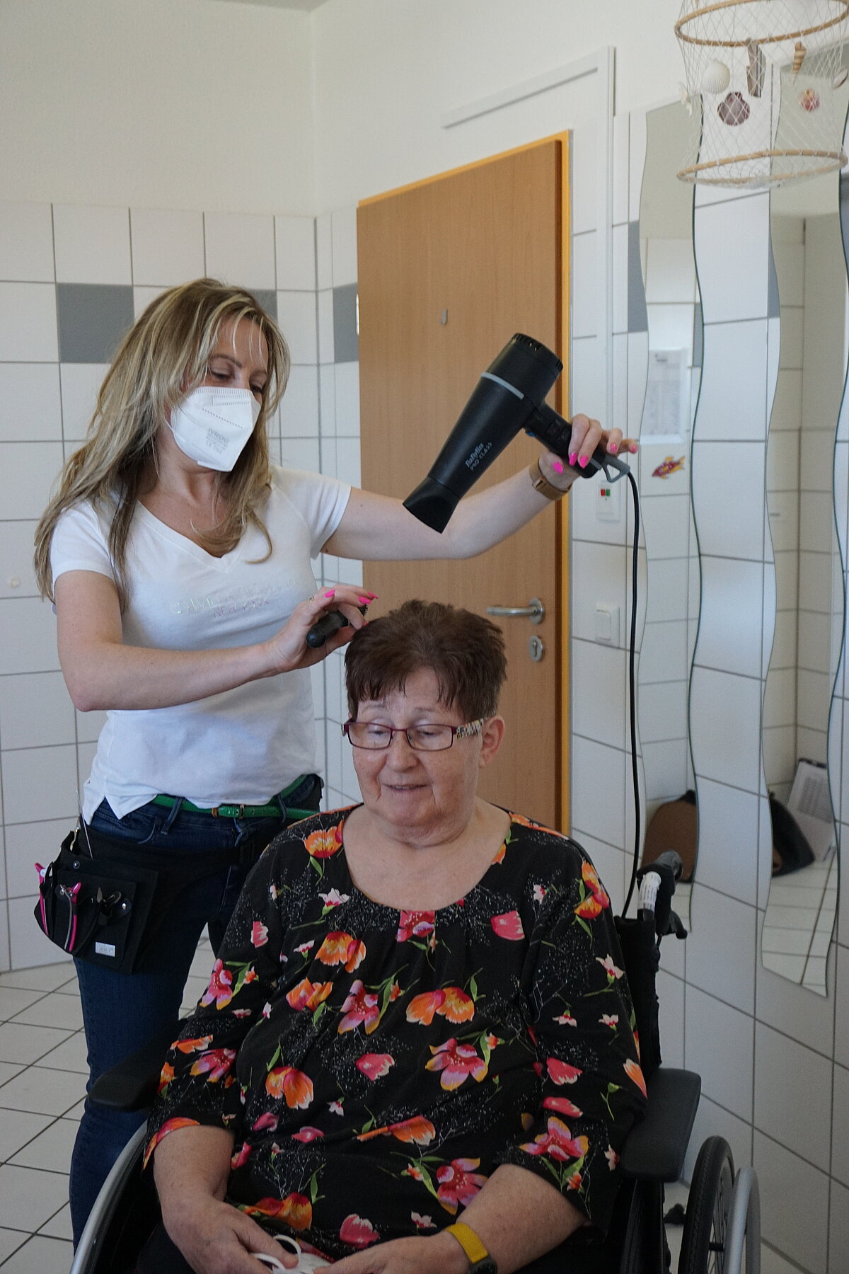 Frisörin föhnt Bewohnerin der Alloheim Senioren-Residenz Fernwald-Annerod die Haare