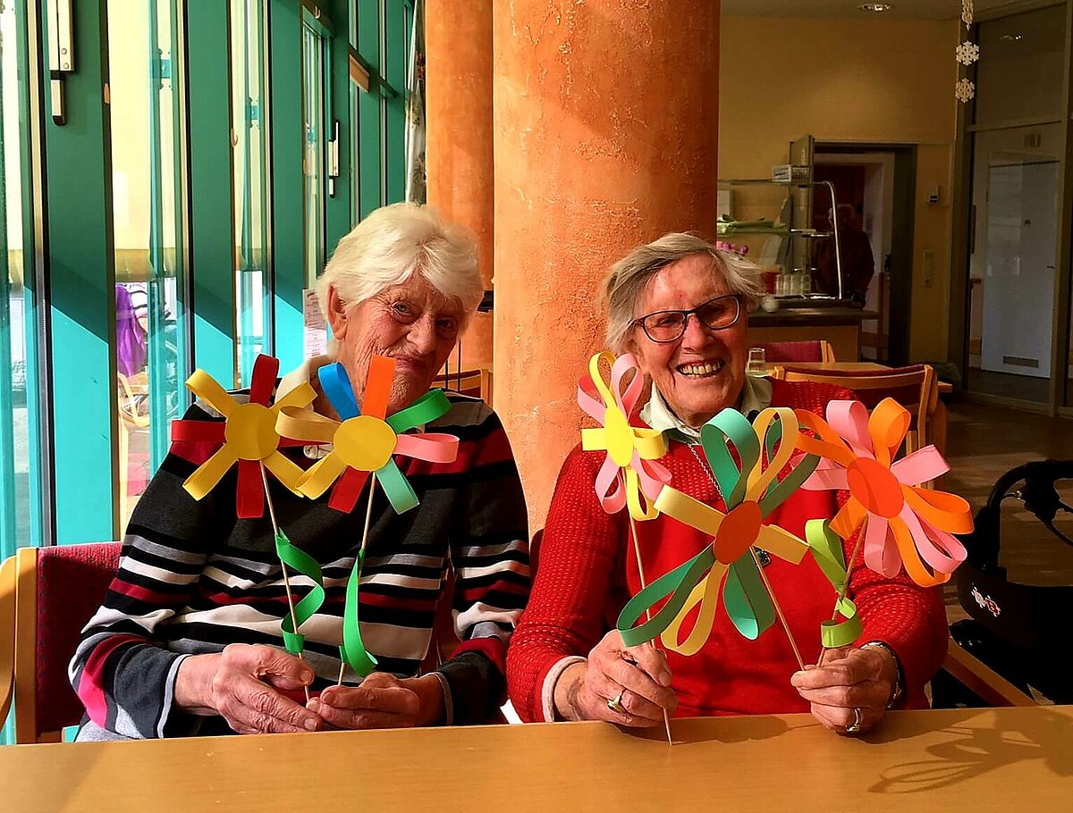 Seniorinnen zeigen selbstgebastelte Blumen aus Pappe