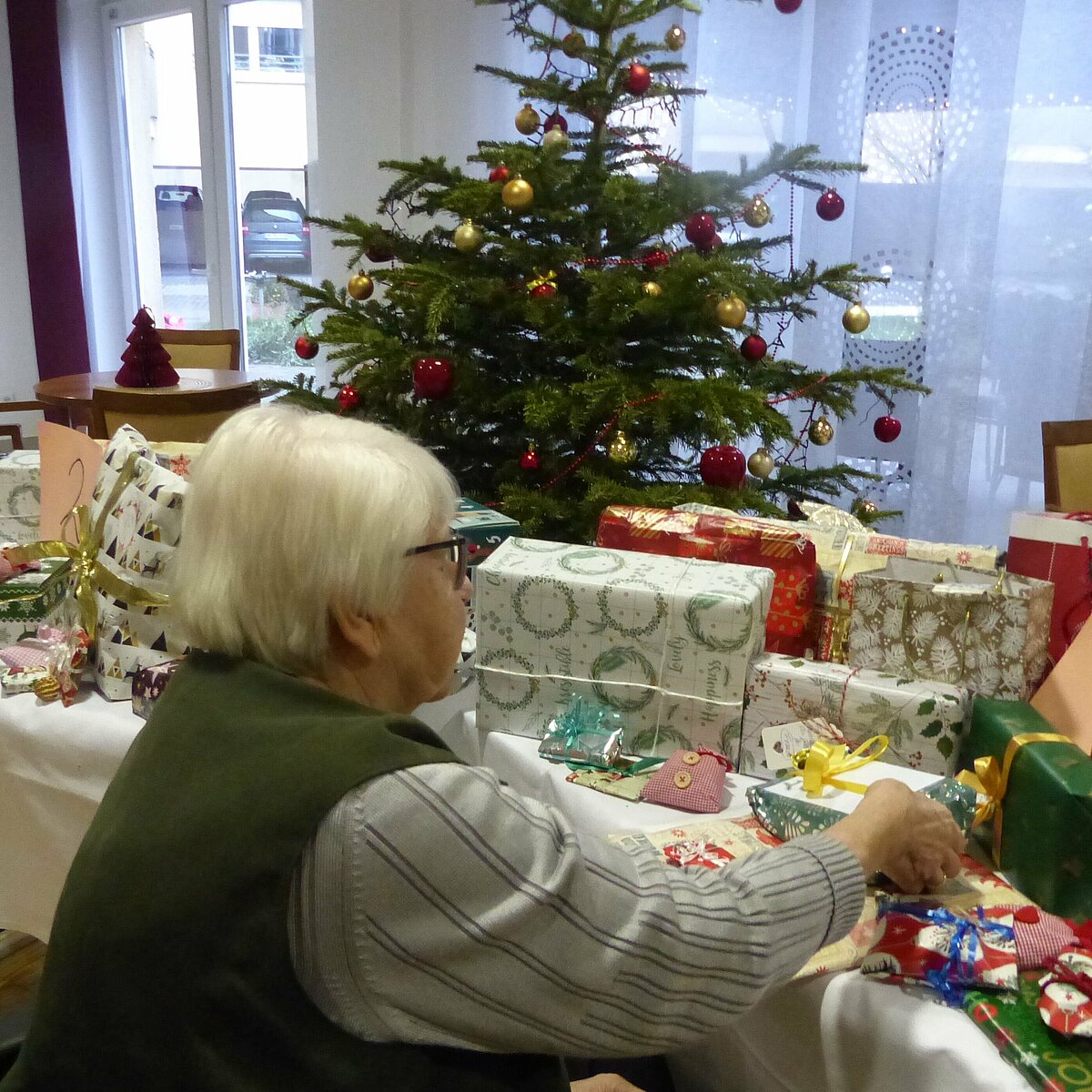 Bewohnerin beim Wichteln vor einem Tisch mit vielen eingepackten Geschenken