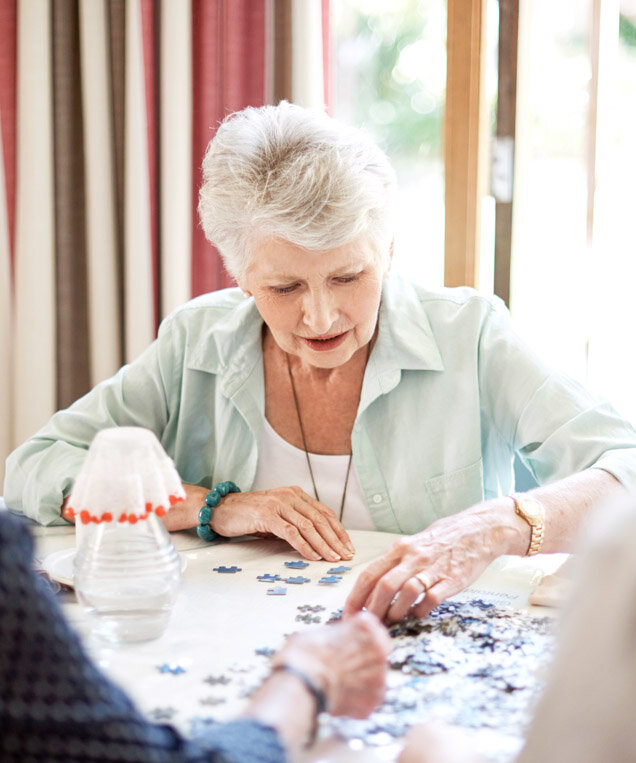 Seniorin mit Demenz puzzelt mit anderen Bewohnern im Pflegeheim