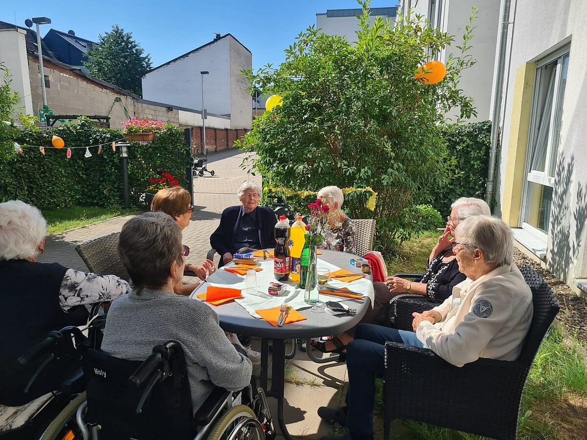 Seniorengruppe sitzt gemeinsam beim Grillfest auf der Terrasse des Pflegeheims AGO Trier