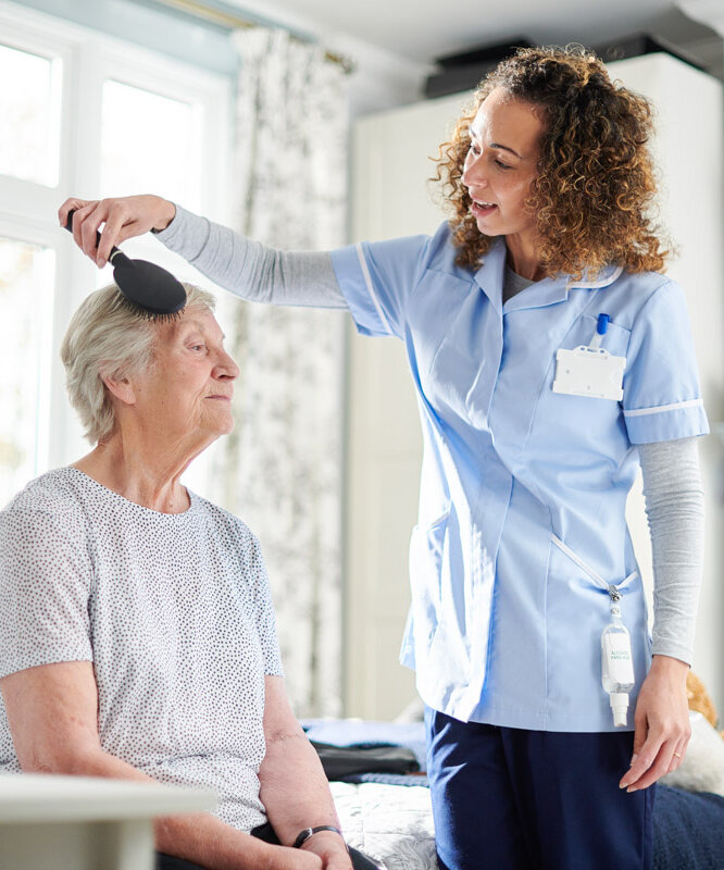 Pflegekraft des ambulanten Pflegedienstes Alloheim Mobil kämmt die Haare einer Seniorin zu Hause