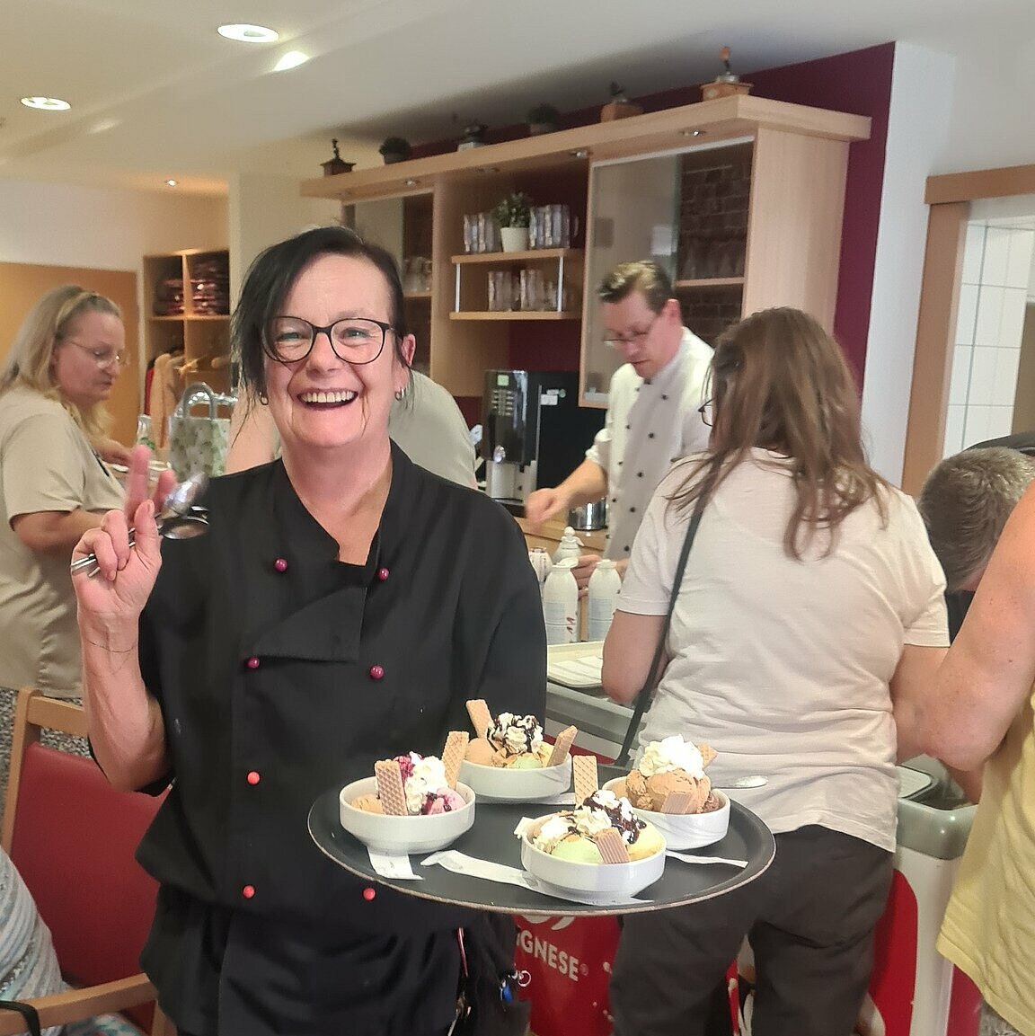 Mitarbeiterin lächelnd mit einem Tablett voller Eisbecher