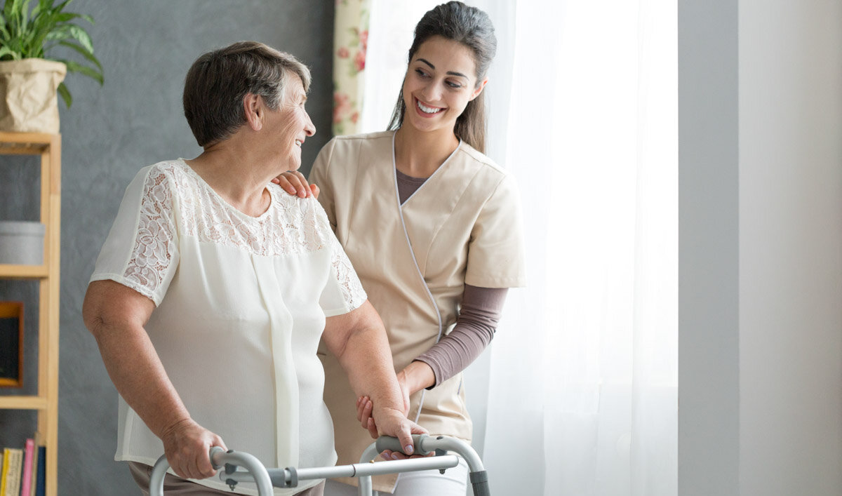 Pflegehilfskraft bei Alloheim hilft Seniorin mit Rollator in einem Altenheim