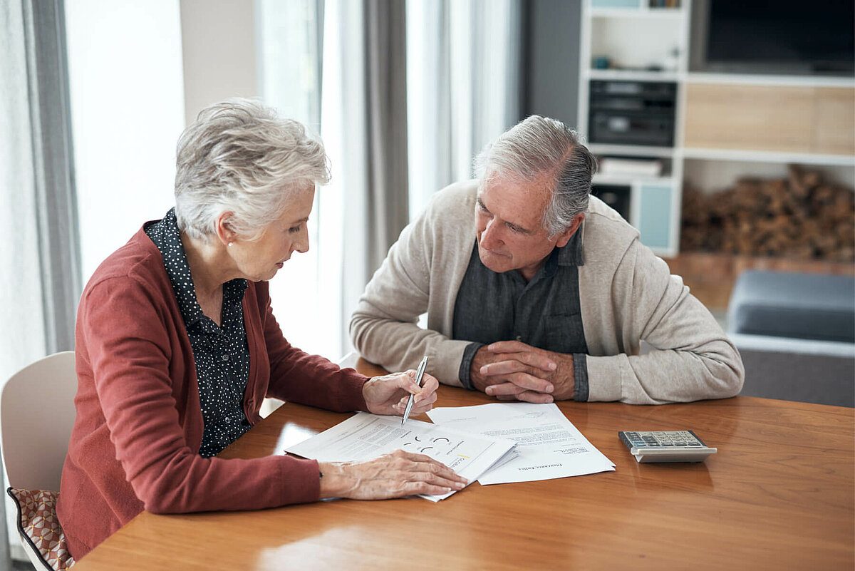 Seniorenehepaar sitzt vor Dokumenten zu Pflegegraden und zur Pflegefinanzierung