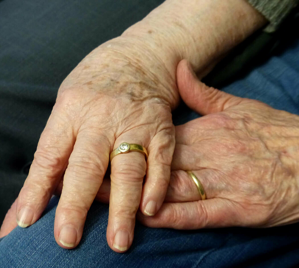 Senioren-Ehepaar legt Hände aufeinander mit Eheringen