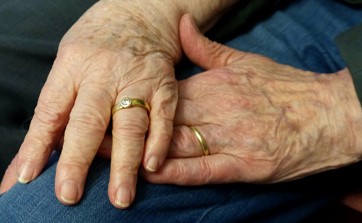 Senioren-Ehepaar legt Hände aufeinander mit Eheringen