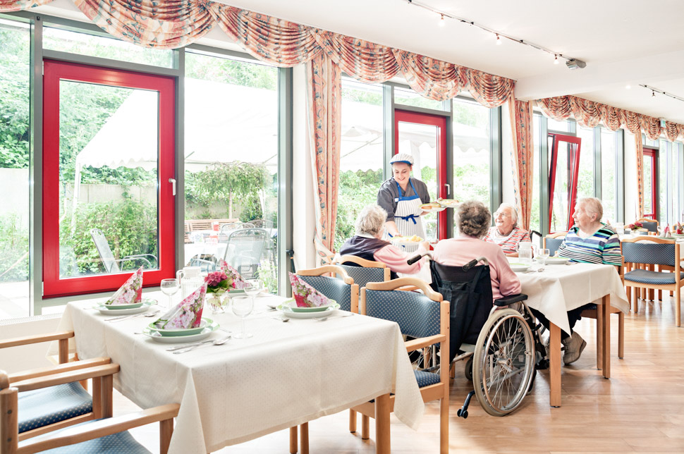 Köchin serviert Bewohnern Essen an den Tisch in der Alloheim Senioren-Residenz Auetalblick in Bad Malente