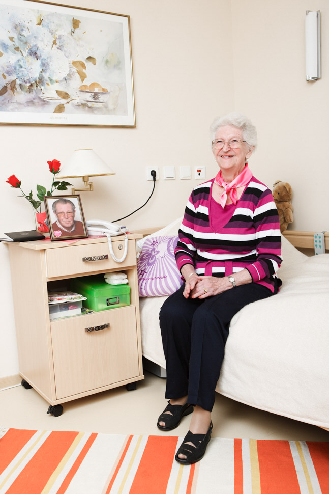 Seniorin sitzt auf Bett in ihrem Zimmer im Alloheim Pflegeheim Anna Margareta in Bad Malente