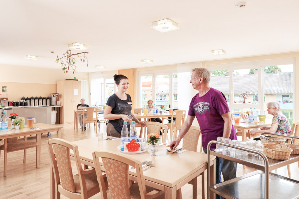 Servicekraft und Bewohner decken Tisch im Speisesaal des Alloheim Seniorenheims Löwenquell in Bad Rodach
