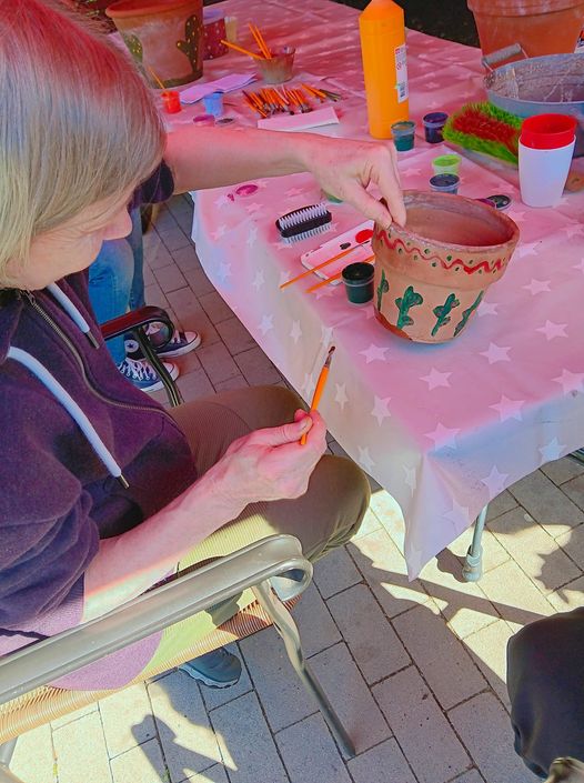 Bewohnerin malt Blumentopf für Gartengruppe an