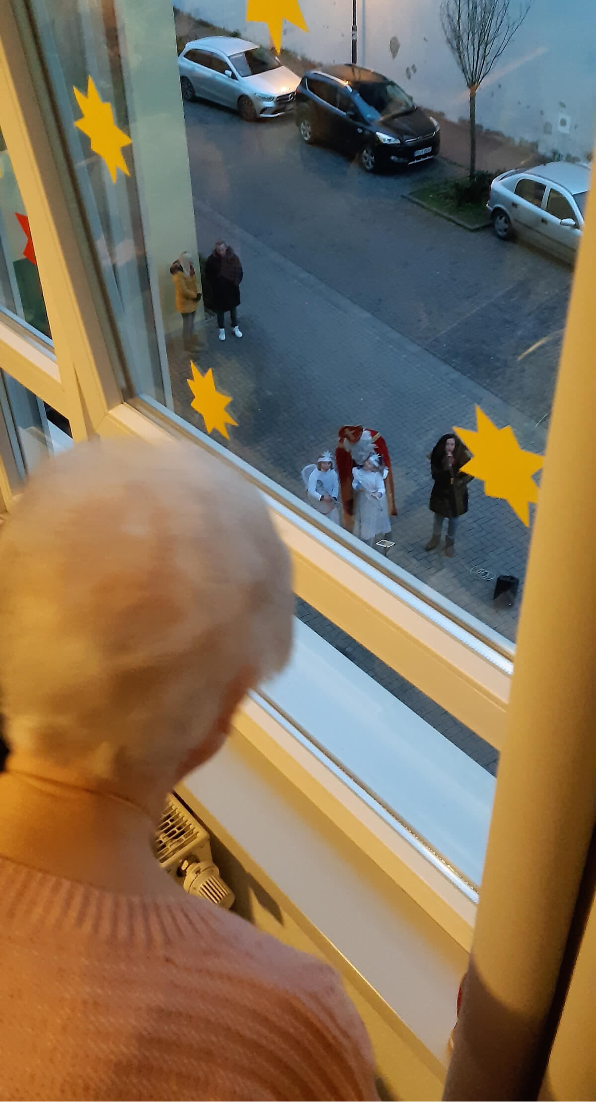 Seniorin schaut vom Fenster aus dem Nikolauskonzert vor der Alloheim Senioren-Residenz Elsdorf zu
