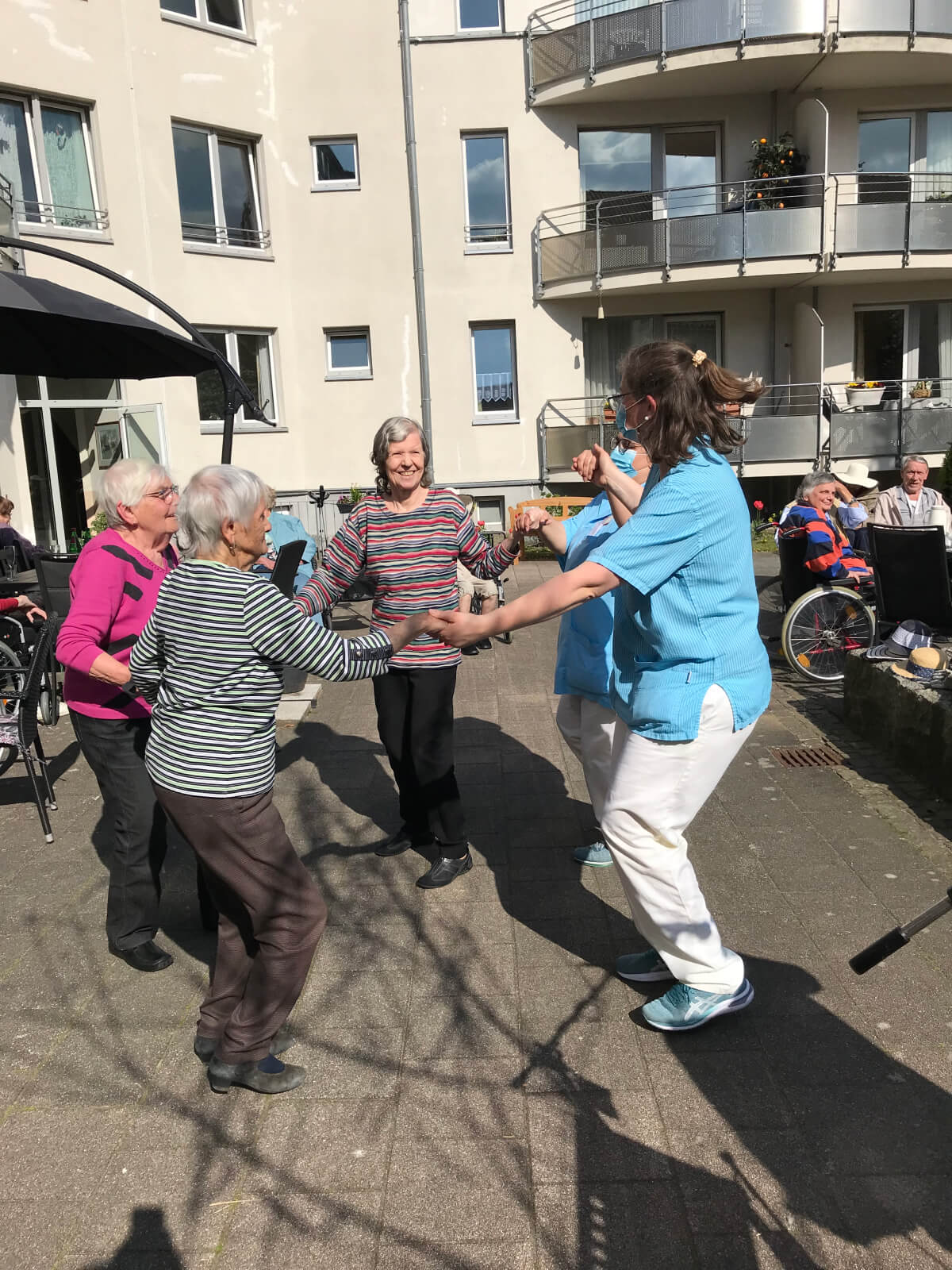 Seniorinnen tanzen mit Betreuungskraft des Altenheims "Waldersee" in Lübeck beim Maifest