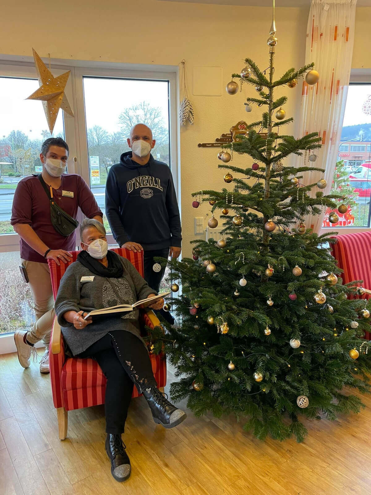Mitarbeiter des Sozialen Dienstes im Pflegeheim AGO Rosbach mit Buch vor dem Weihnachtsbaum