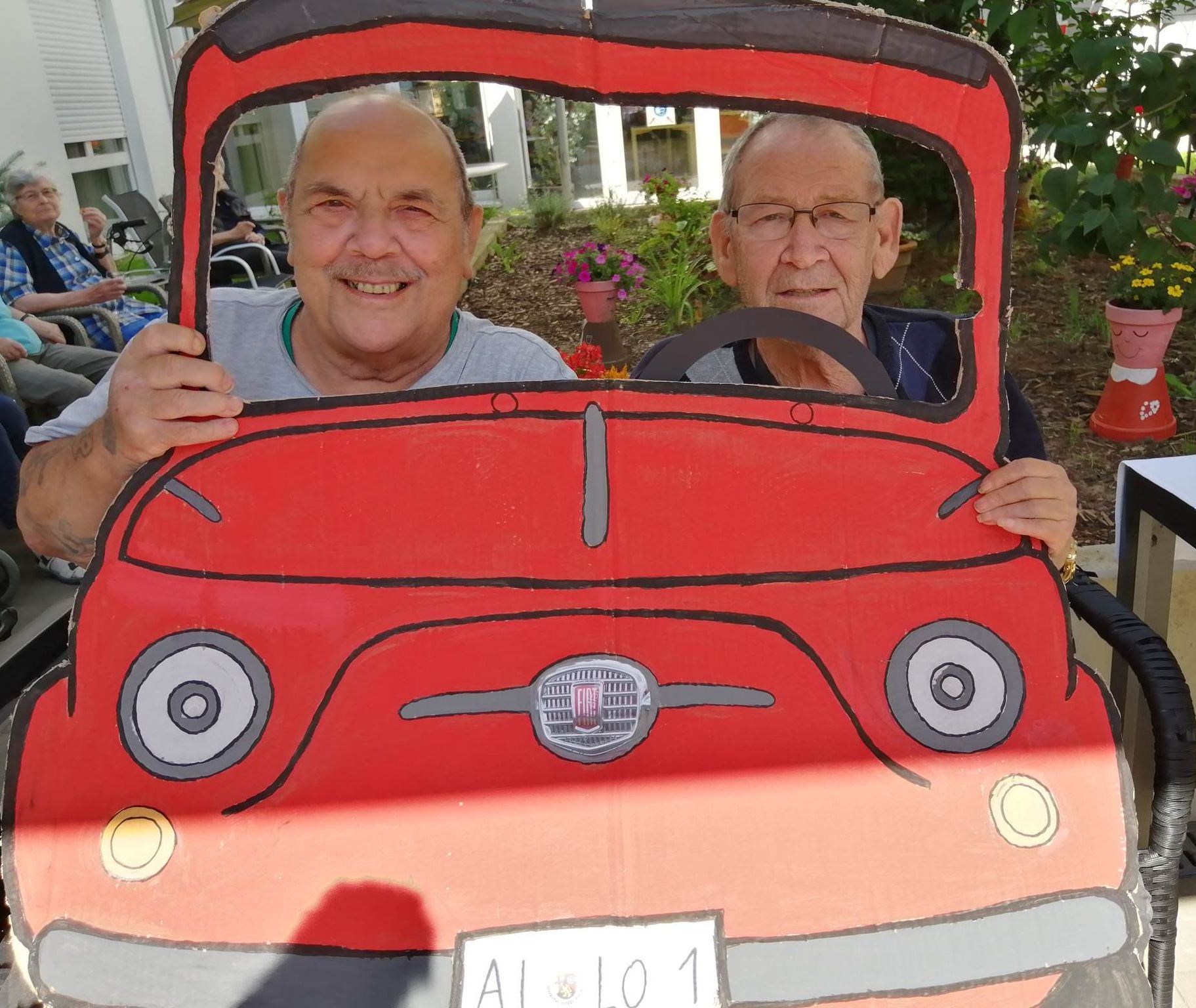 Bewohner hinter Papp-Auto bei der italienischen Woche - Dolomiten im Seniorenzentrum AGO Trier 