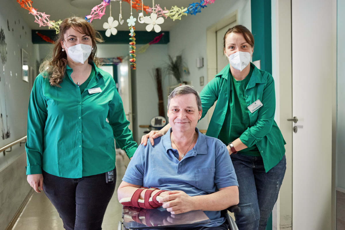 Pflegekräfte schieben Bewohner im Rollstuhl in einem Alloheim Pflegeheim