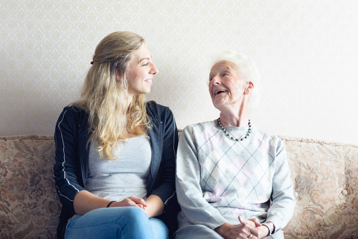 Praktikantin sitzt mit Seniorin auf der Couch in einem Alloheim Pflegeheim