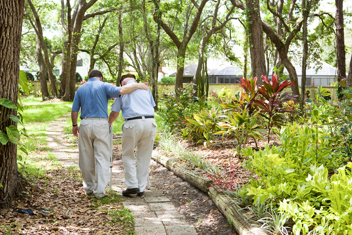 Pfleger geht mit Bewohner im Garten eines speziellen Alloheim Pflegeheims für Demenzkranke spazieren