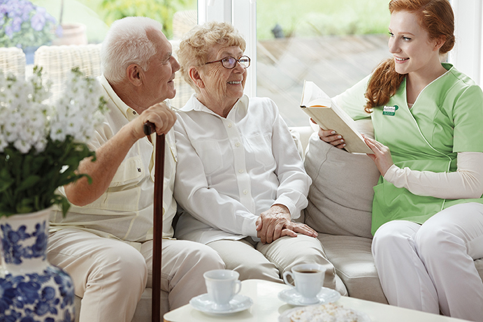 Pflegekraft sitzt mit Bewohner-Ehepaar auf der Couch einer Alloheim Senioren-Residenz