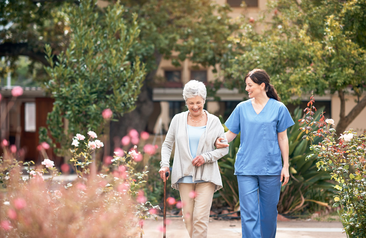 Pflegerin geht mit Bewohnerin spazieren im Garten eines Alloheim Pflegeheims mit stationärer Langzeitpflege