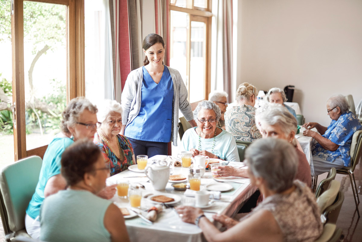 Pflegekraft zusammen mit Gästen der Tagespflege bei Alloheim am Mittagstisch beim Essen